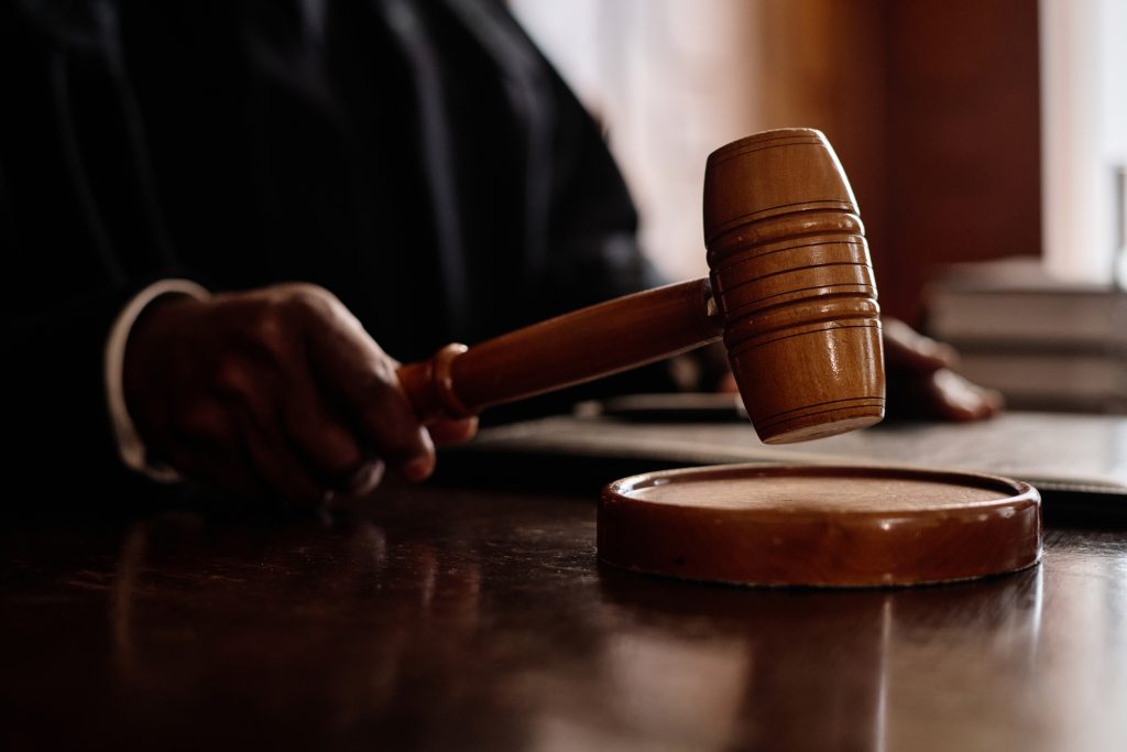 Focus on wooden gavel held by impartial judge sitting by desk and announcing verdict to suspect during trial session in courtroom